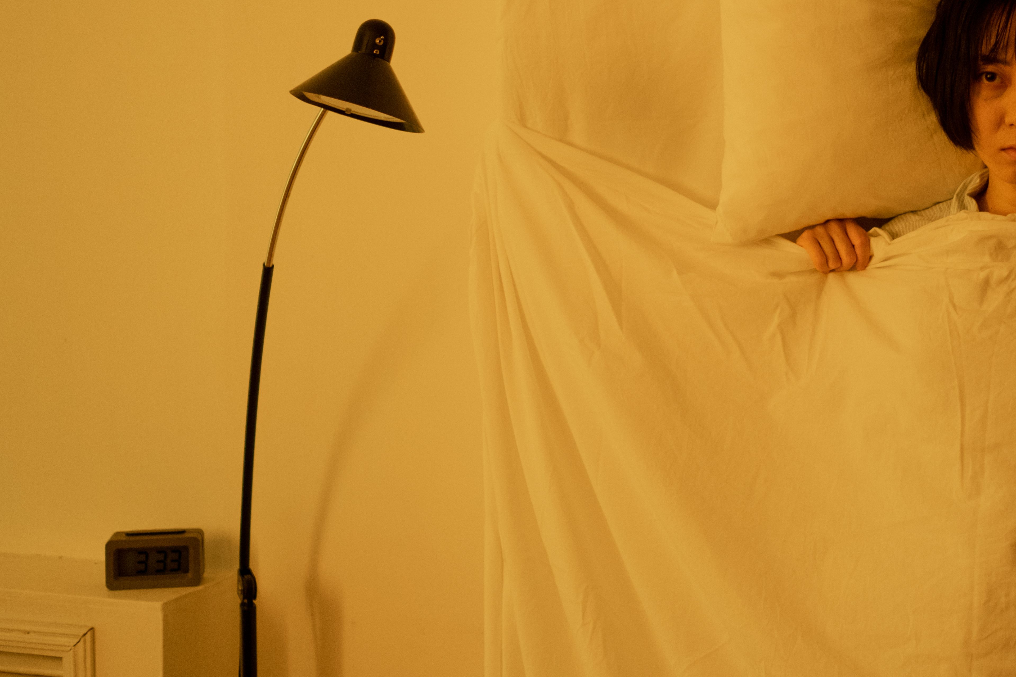 A person lies quietly in soft bedroom light — conveying the experience of sleep that does not come easily, and the mental health consequences that follow.