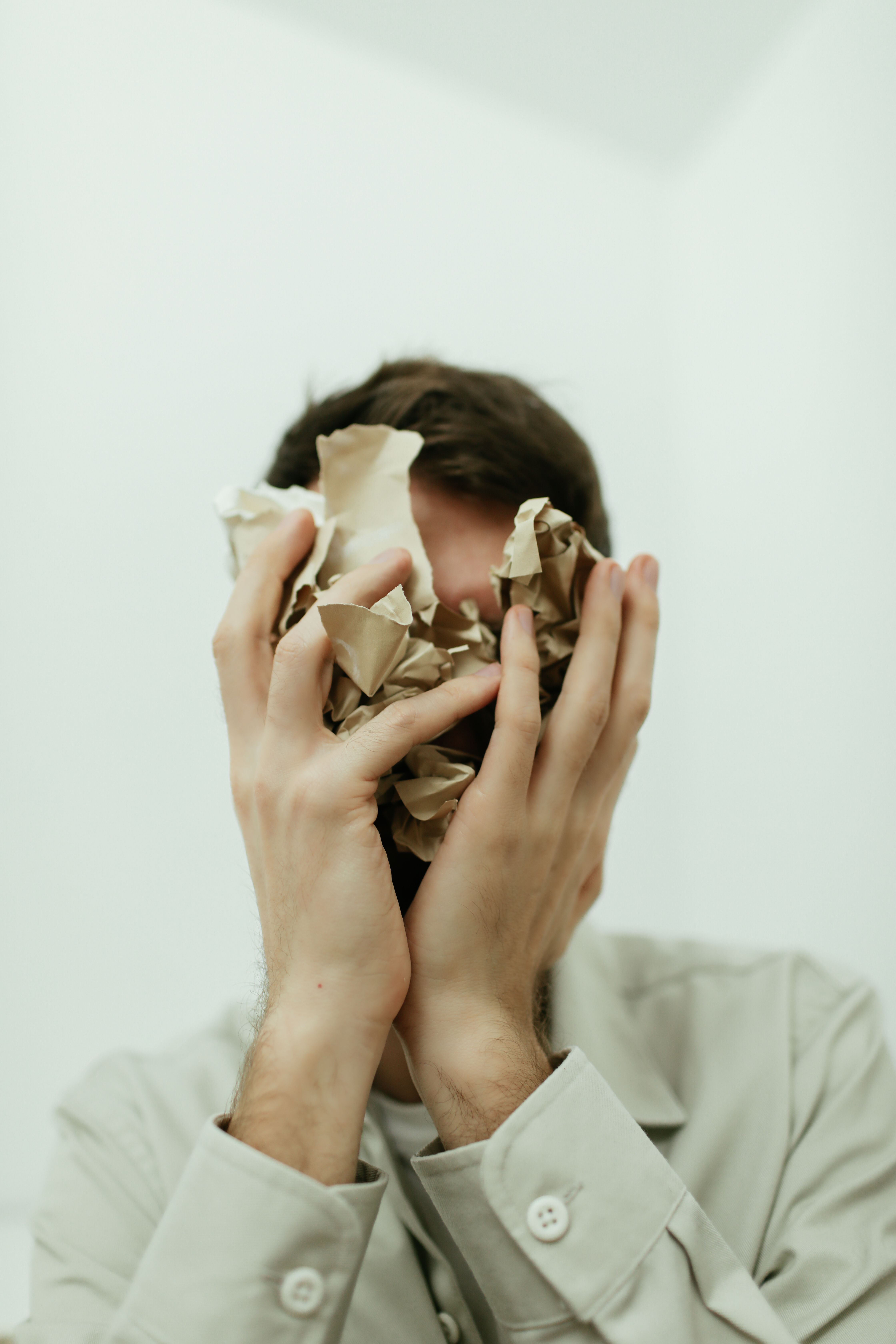 A person holds crumpled paper in front of their face against a pale background — conveying the internal overwhelm and obscured clarity that characterises chronic stress.